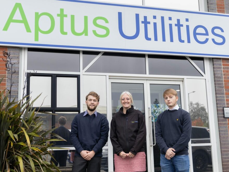 The image showcases a partnership between Aptus Utilities and Bolton College, featuring two T Level students, Tom Daly and Ryan James, alongside Natasha Clarke, the People Director of Aptus Utilities. They stand before the company's headquarters, easily identified by the prominent "Aptus Utilities" sign. This photo emphasises the company's initiative to offer industry placements for students, fostering a hands-on learning environment and potential career opportunities within the utilities sector.